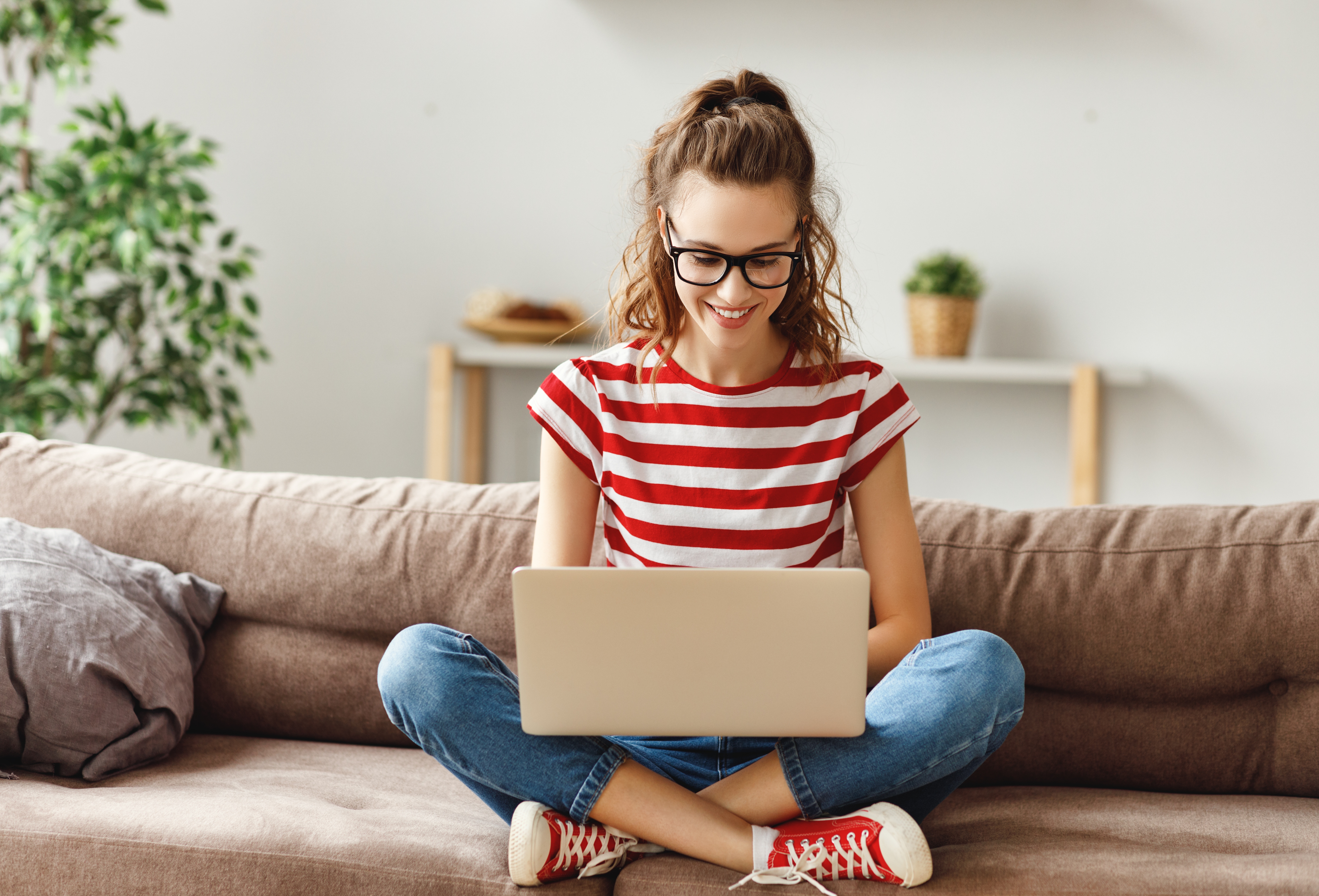 Eine junge Frau sitzt mit ihrem Laptop auf einem Sofa.